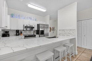 A modern kitchen with white cabinetry, a marble countertop, a stainless steel refrigerator, and a coffee maker.