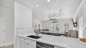 A modern kitchen with white cabinetry, a marble countertop, and a built-in dishwasher. - Destined to Be - Beach Cottage with Private Pool & Guest House (Destin)