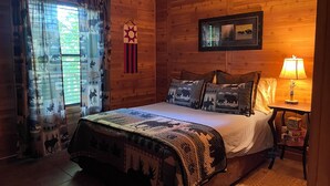 A cozy log cabin bedroom with a bed, pillows, a nightstand, a lamp, and a ceiling fan. - Secluded yet within minutes of your favorite outdoor activities!! (Marshall)