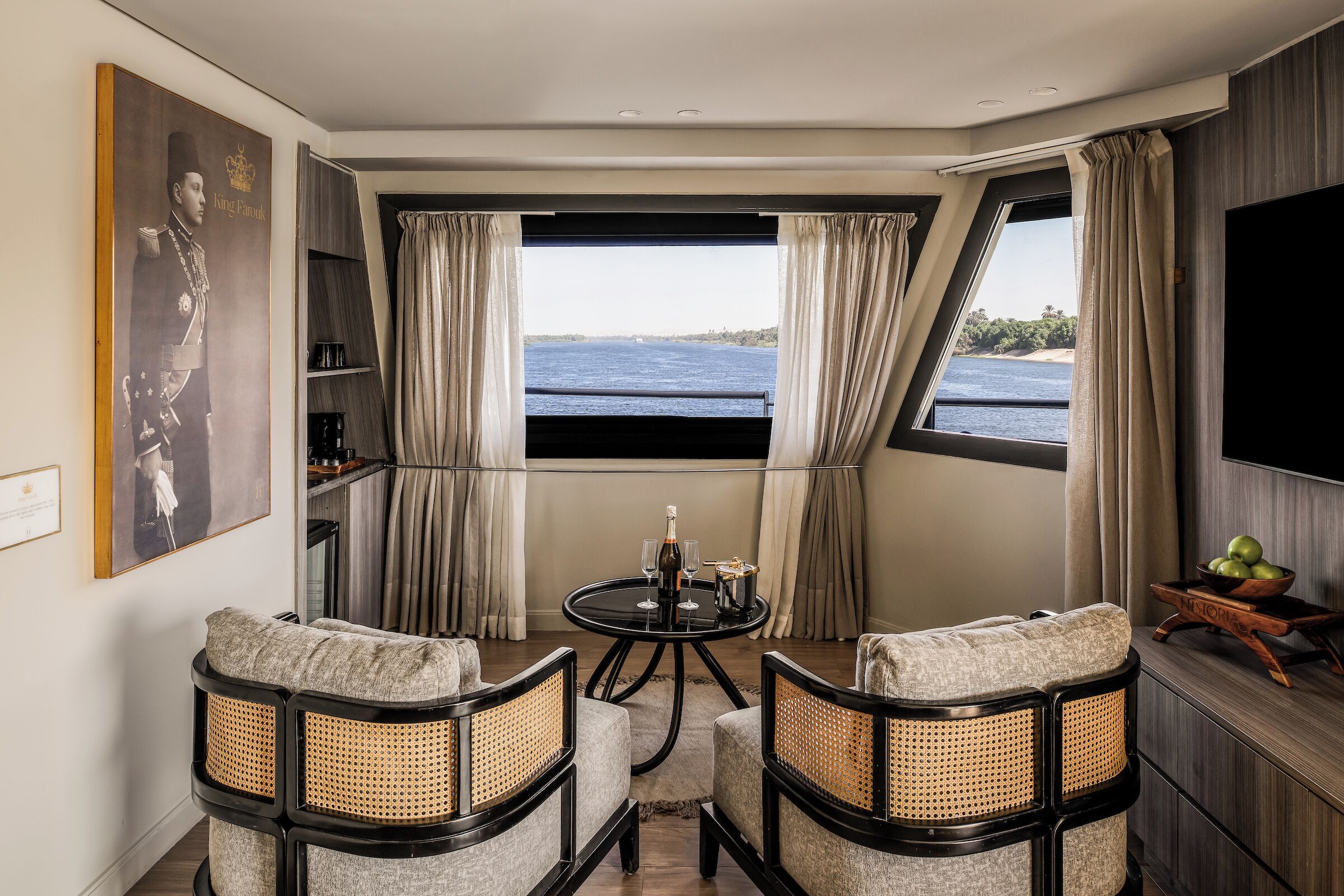 A room with a round table, two chairs, a television, and a window with curtains.