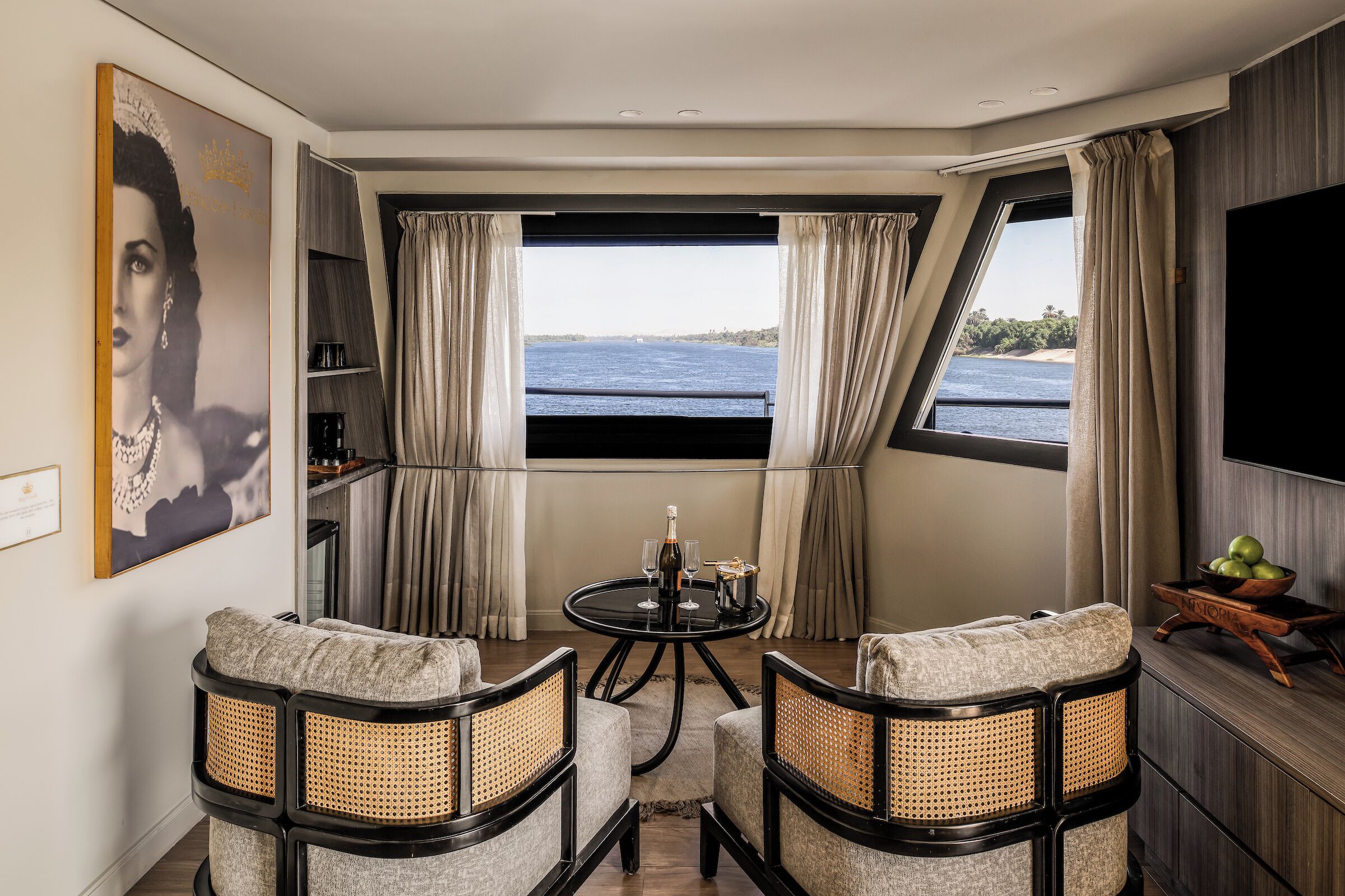 A room with a round table, two chairs, a TV, a bookshelf, and a window with curtains.