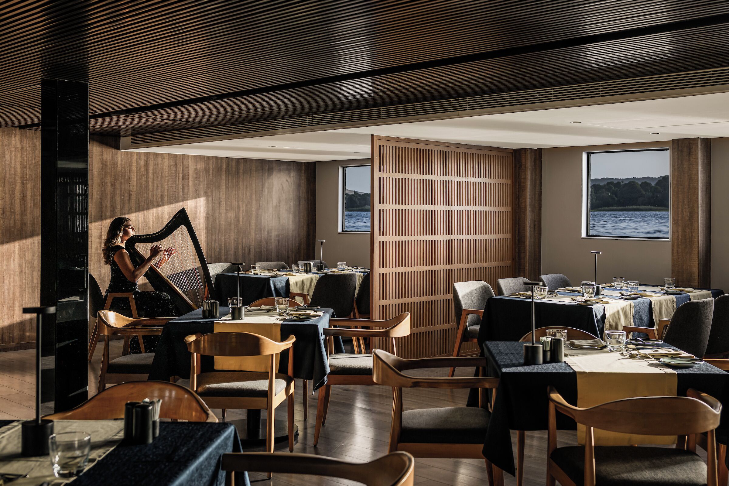 Un restaurant avec des meubles en bois, des tables dressées pour le repas et une vue sur l’eau.