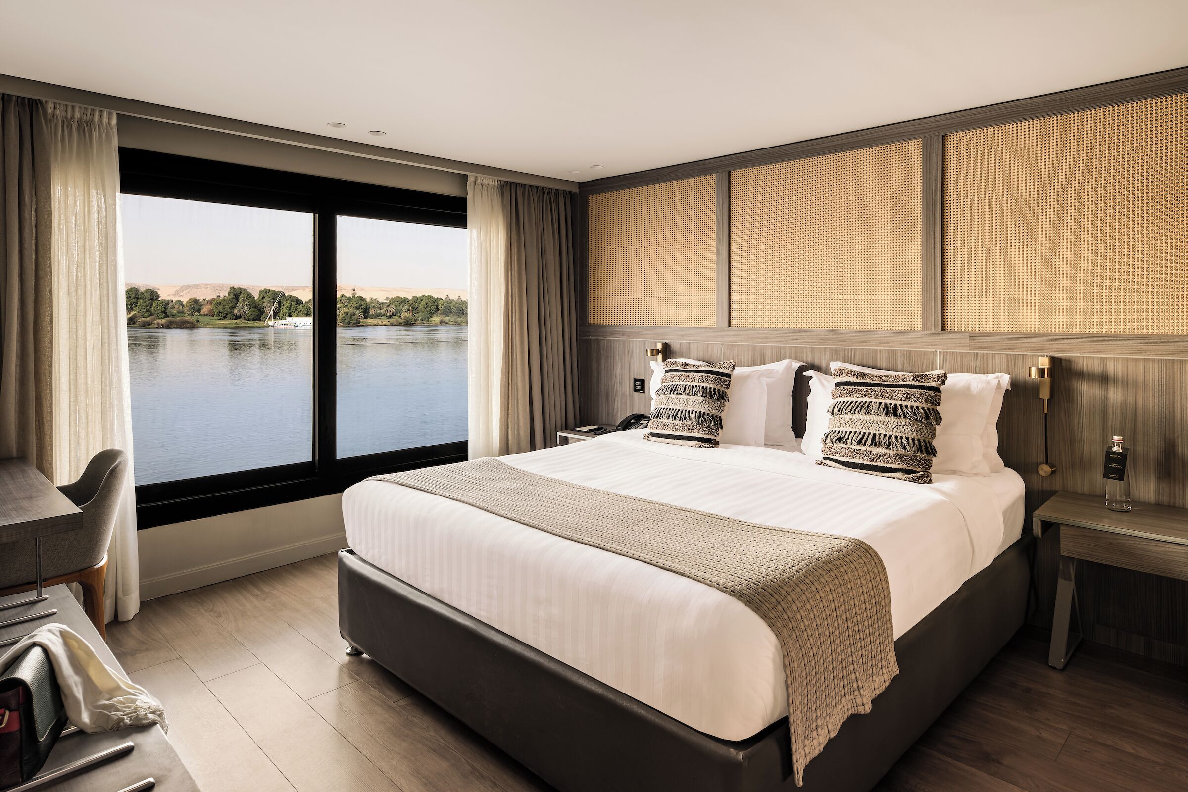 A modern hotel room with a large bed, a desk, and a view of a lake.
