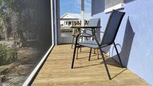 En træterrasse med to stole og et bord, en glasdør der fører ud, samt udsigt til en bygning i baggrunden.