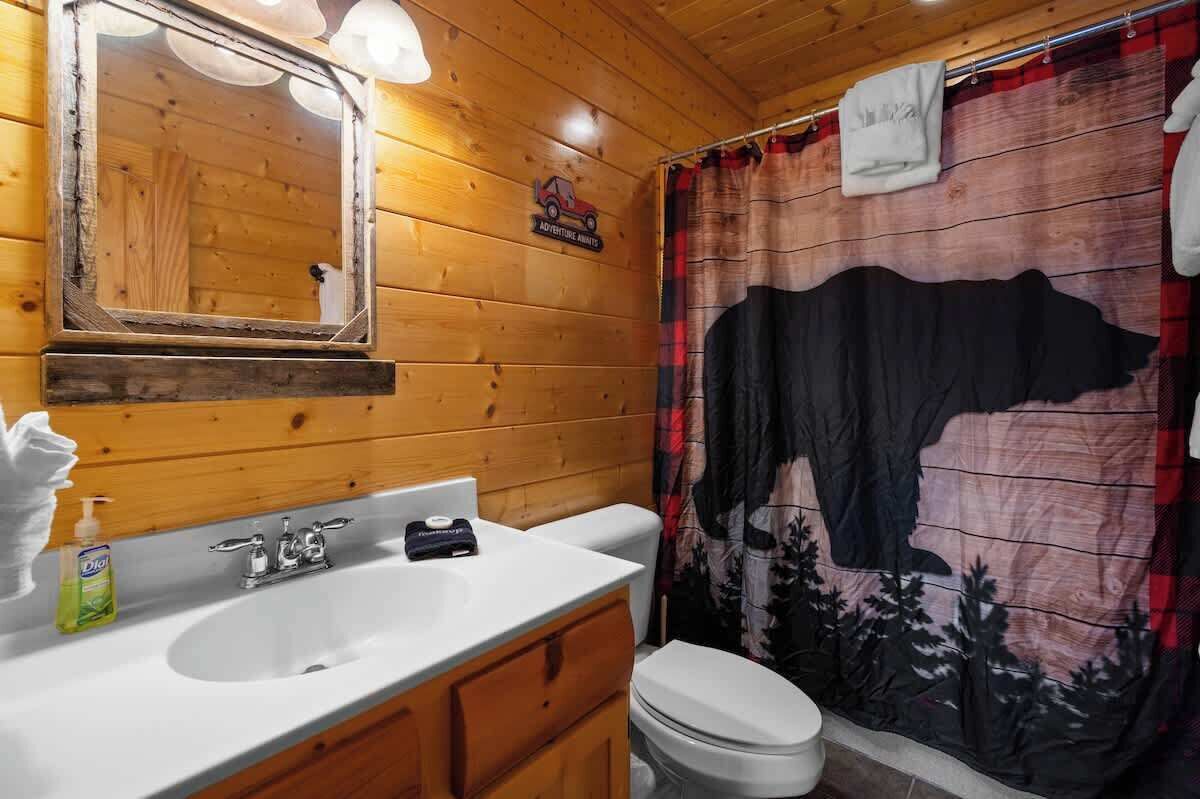 Een houten badkamer met een wastafel, spiegel en douchegordijn waarop een koe en bomen afgebeeld zijn.