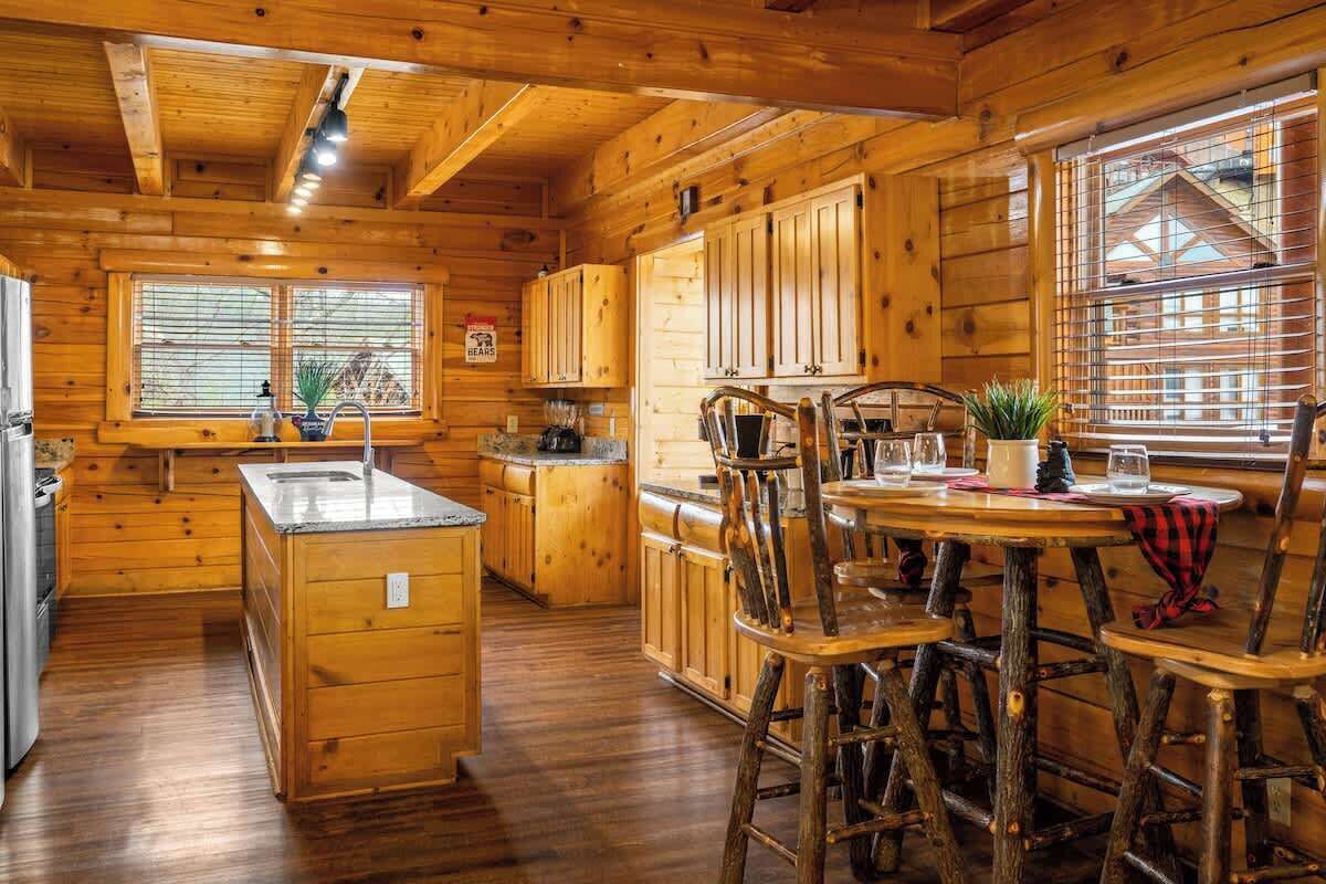 A log cabin interior with a kitchen, dining area, and a large window.