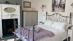 Ein Schlafzimmer mit Bett, Nachttisch, Kommode, Spiegel, Kamin und einem Bild an der Wand.