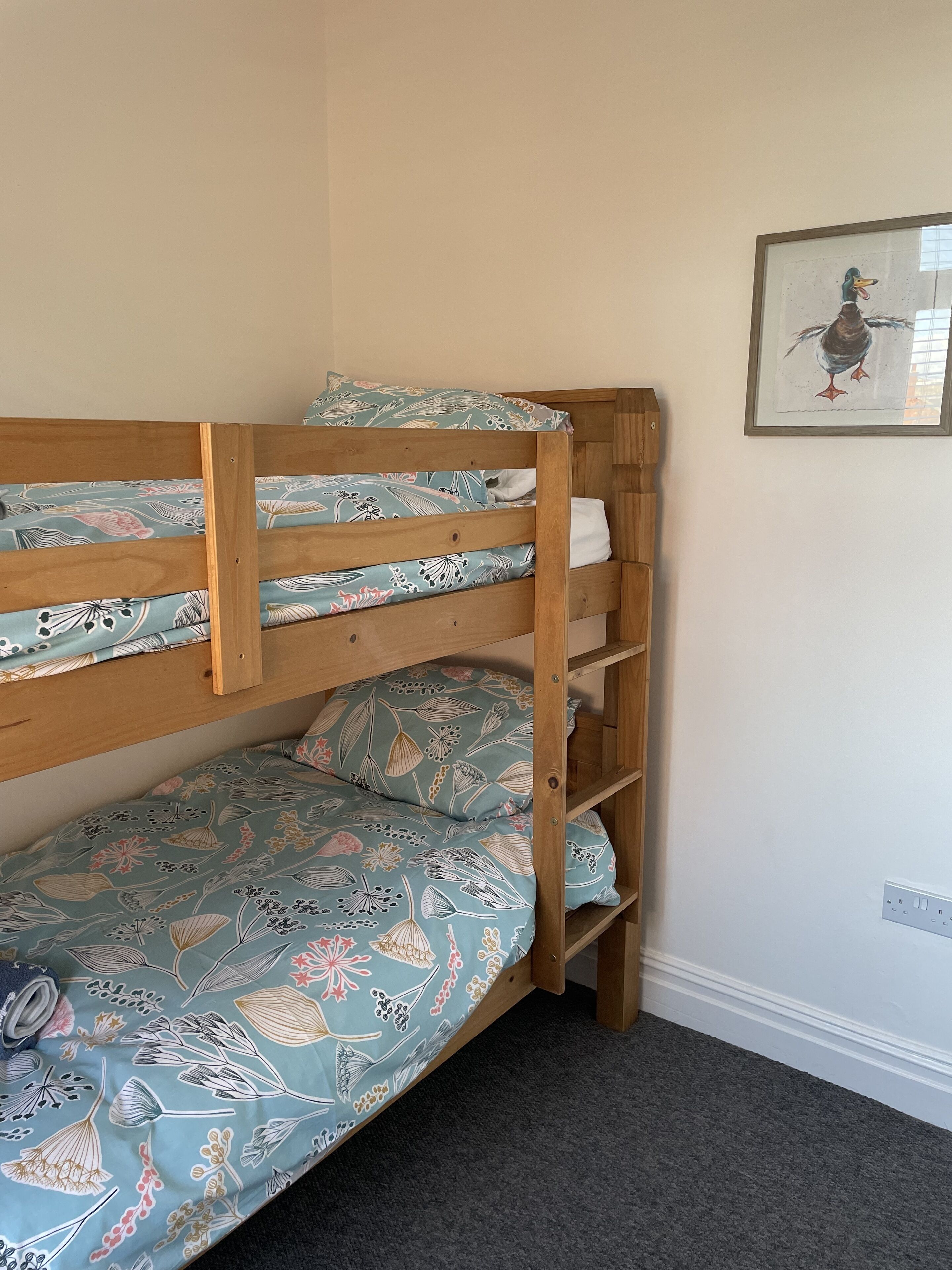 A bunk bed with floral bedding, a wooden headboard, and a framed picture on the wall.