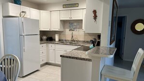 A kitchen with white cabinets, a refrigerator, a sink, and a dining area with chairs. - Canal Suite with Water views (Saint James City)