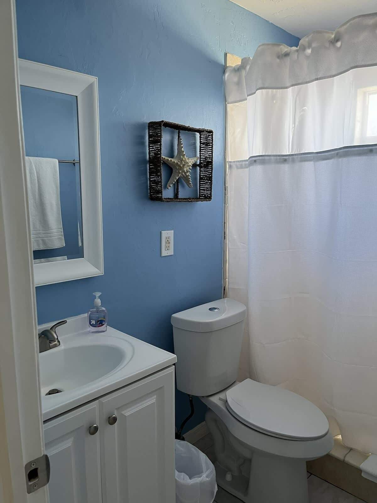 Un baño con pared azul, lavamanos blanco, inodoro, decoración de estrella de mar y cortina de ducha.