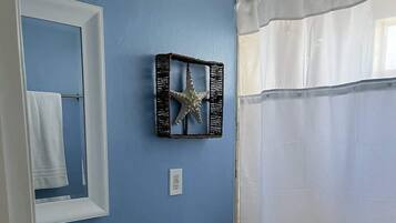 Un baño con pared azul, lavamanos blanco, inodoro, decoración de estrella de mar y cortina de ducha.