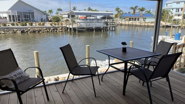 A wooden deck with a table and chairs overlooking a marina with boats and buildings. - Canal Suite with Water views (Saint James City)