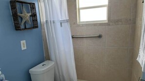 A bathroom with a toilet, a shower with a glass door, a towel rack, and a starfish decoration on the wall. - Canal Suite with Water views (Saint James City)