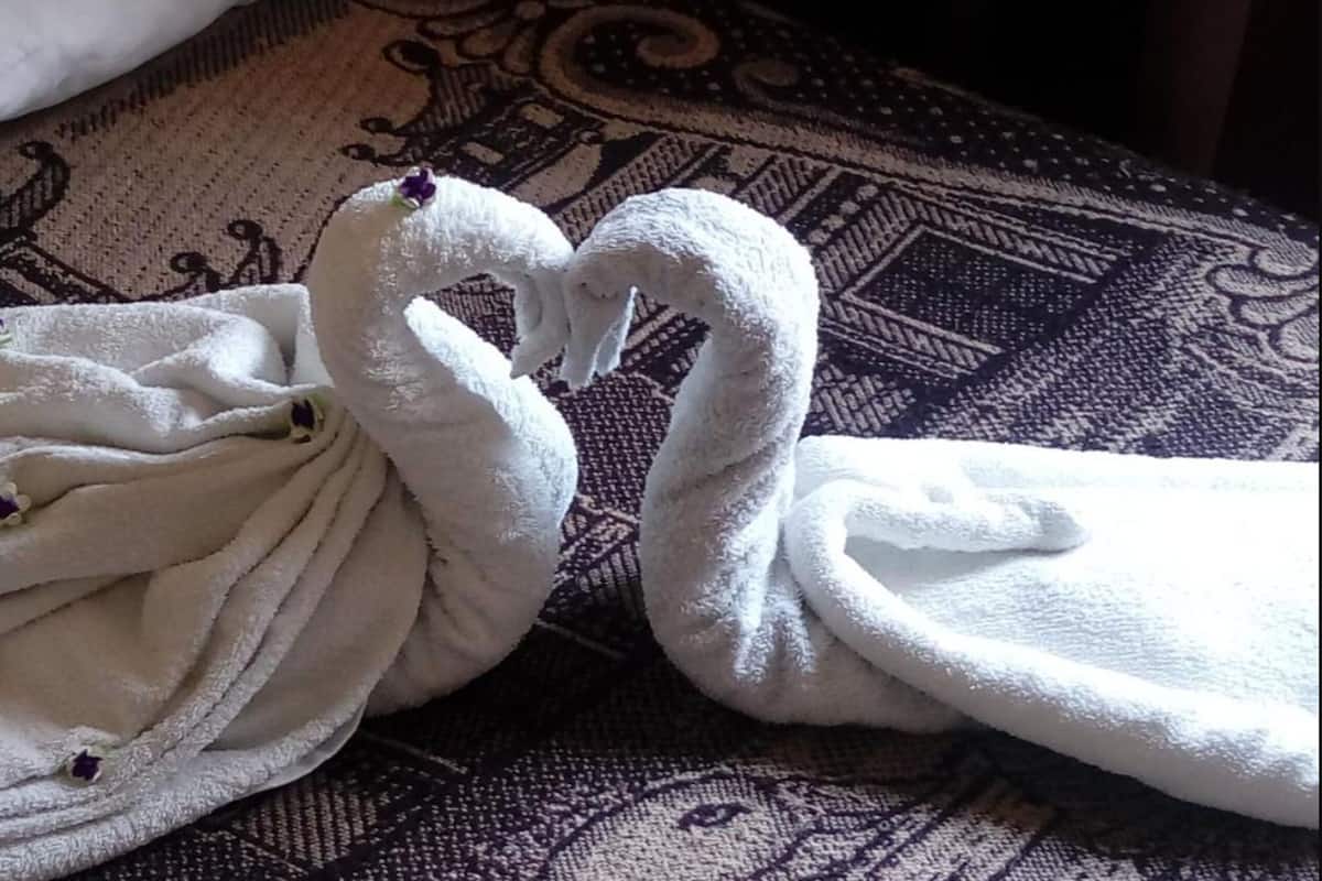 A bed with white towels arranged in a swan shape.
