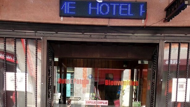 A hotel entrance with a digital sign, glass doors with red Chinese characters, and a manhole cover on the pavement. - Hotel Patria (Mexico City)