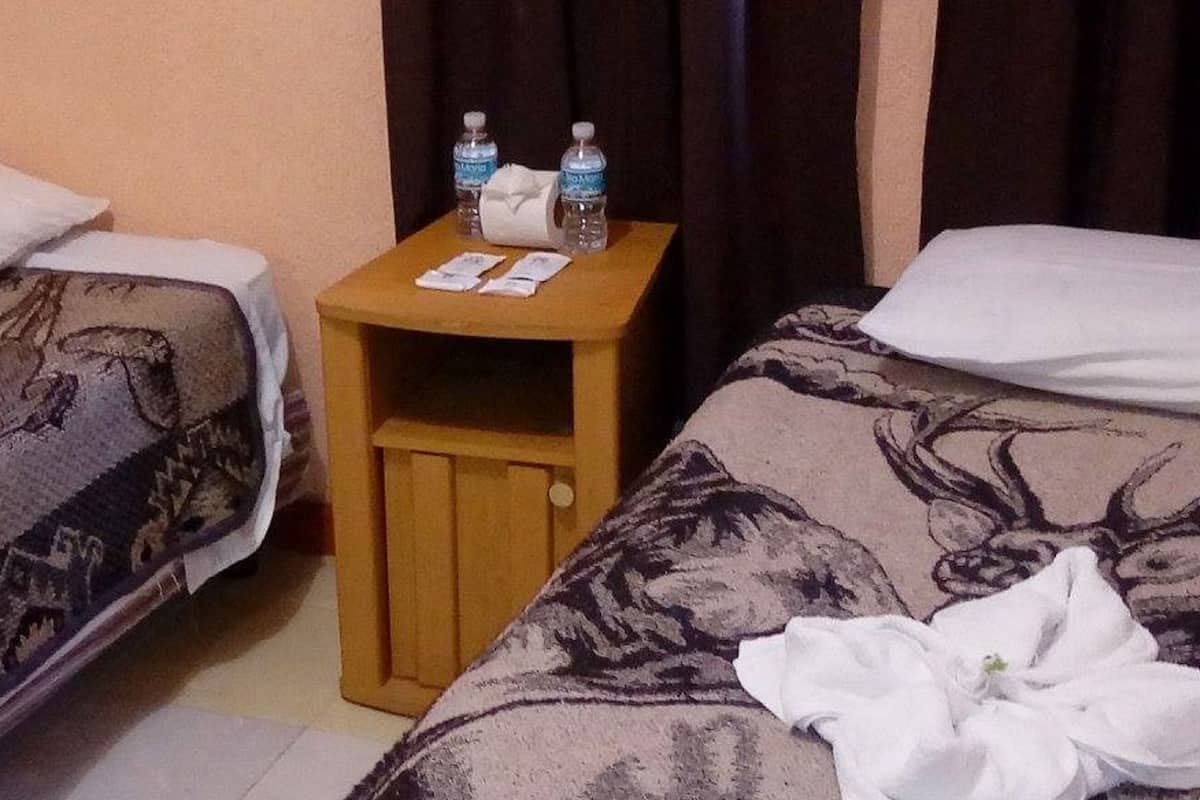 A hotel room with two beds, a wooden nightstand with toiletries, and a patterned bedspread.