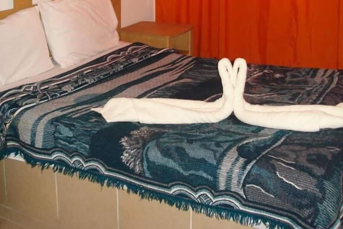 A hotel room with a bed, a wooden headboard, a nightstand, and an orange curtain.