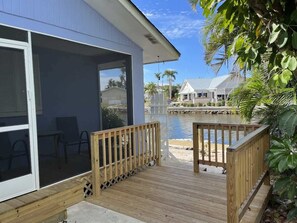 A wooden deck leading to a glass door, a pool, and a white building with a covered patio area.