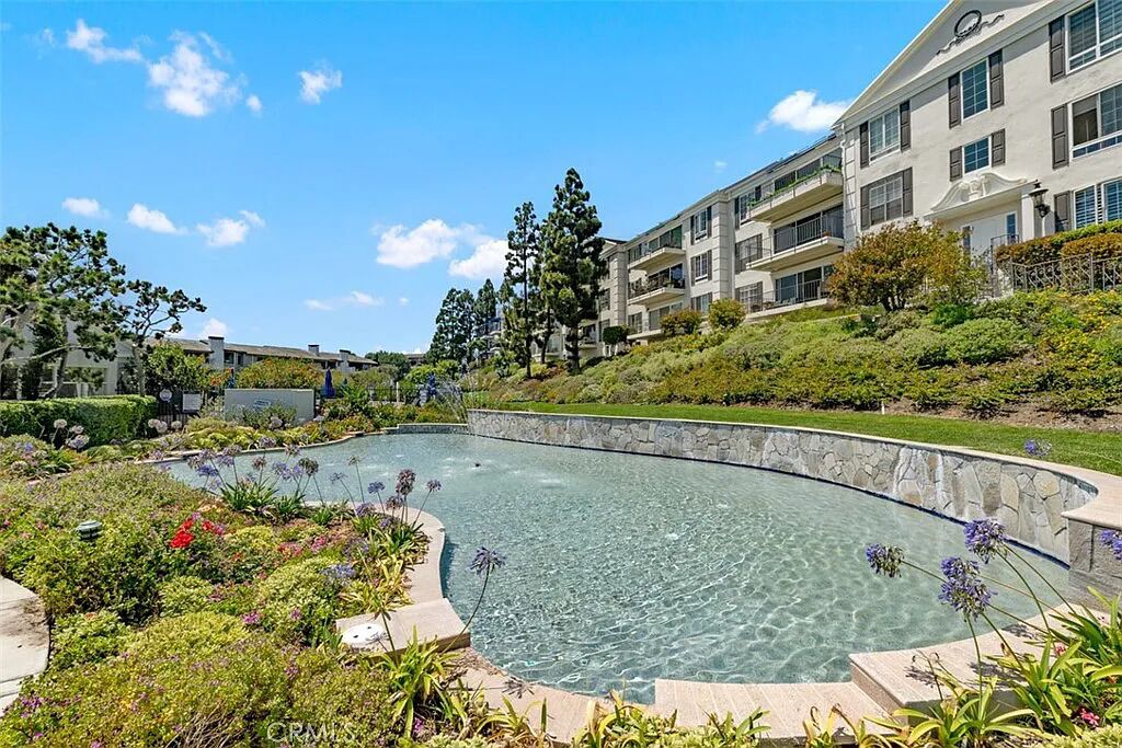 Un hotel con piscina rodeado de jardines ajardinados y un edificio de varios pisos con balcones.