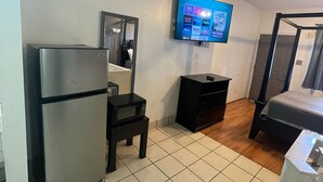 A compact hotel room with a kitchenette, a bed, a TV mounted on the wall, and a small table. - Best Budget Inn (Bastrop)