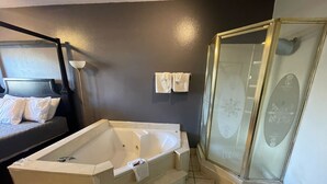 A modern bathroom with a large bathtub, a glass shower enclosure, and a bed with a headboard. - Best Budget Inn (Bastrop)