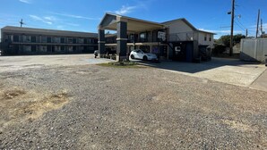 A building with a covered parking area, a basketball hoop, and a white car parked outside. - Best Budget Inn (Bastrop)