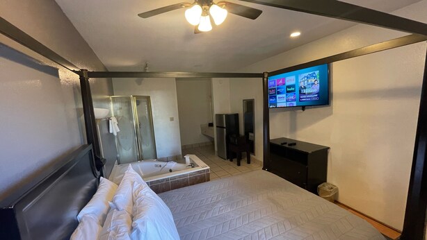 A hotel room with a bed, a shower, a TV mounted on the wall, and a ceiling fan. - Best Budget Inn (Bastrop)