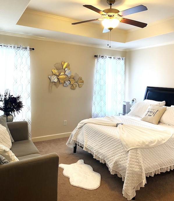 A bedroom with a bed, a chair, a ceiling fan, and a wall decoration.