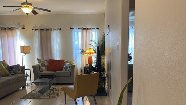 Un soggiorno con divano, poltrone, tavolino, televisore, lampada e ventola a soffitto.