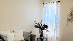 Una camera da letto con un letto, una ventola a soffitto, una finestra con tende, un tavolino con un vaso di fiori e un divano con cuscini.