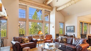 A spacious living room with leather sofas, a glass coffee table, and large windows offering a view of the outdoors.