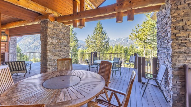 A wooden deck with a round table and chairs, stone walls, and a view of mountains.