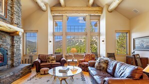 A cozy living room with leather sofas, a stone fireplace, and large windows offering mountain views.