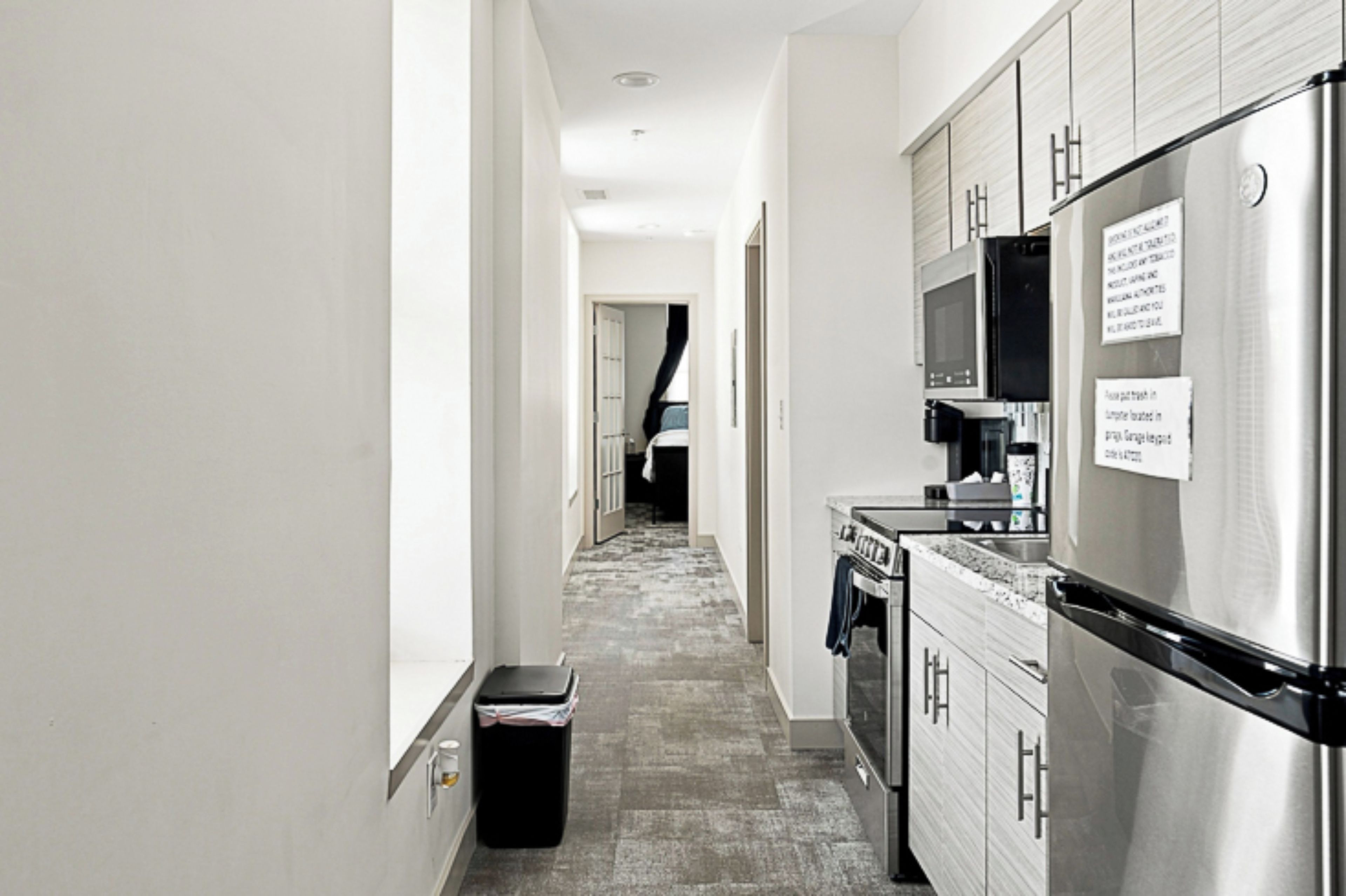 A narrow kitchen with stainless steel appliances, a trash bin, and a microwave.