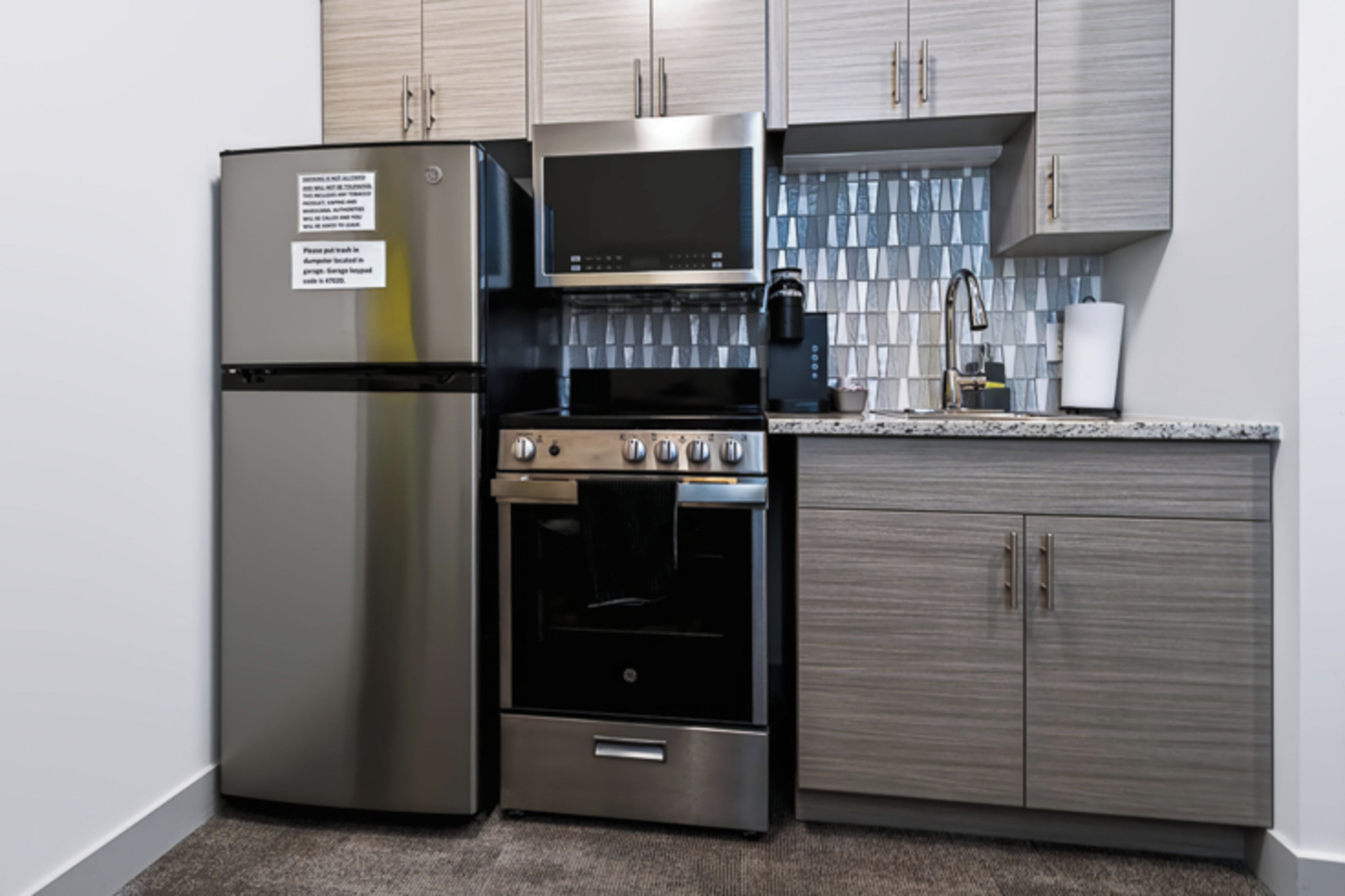 A kitchen with stainless steel appliances, including a refrigerator, microwave, and oven, with wooden cabinets and a tiled backsplash.