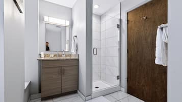 A modern bathroom with a shower, a vanity with a mirror, and a wooden door.