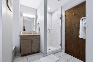 A modern bathroom with a shower, a vanity with a mirror, and a wooden door. - Downtown Historic Warehouse District Lofts 206 (Cleveland)