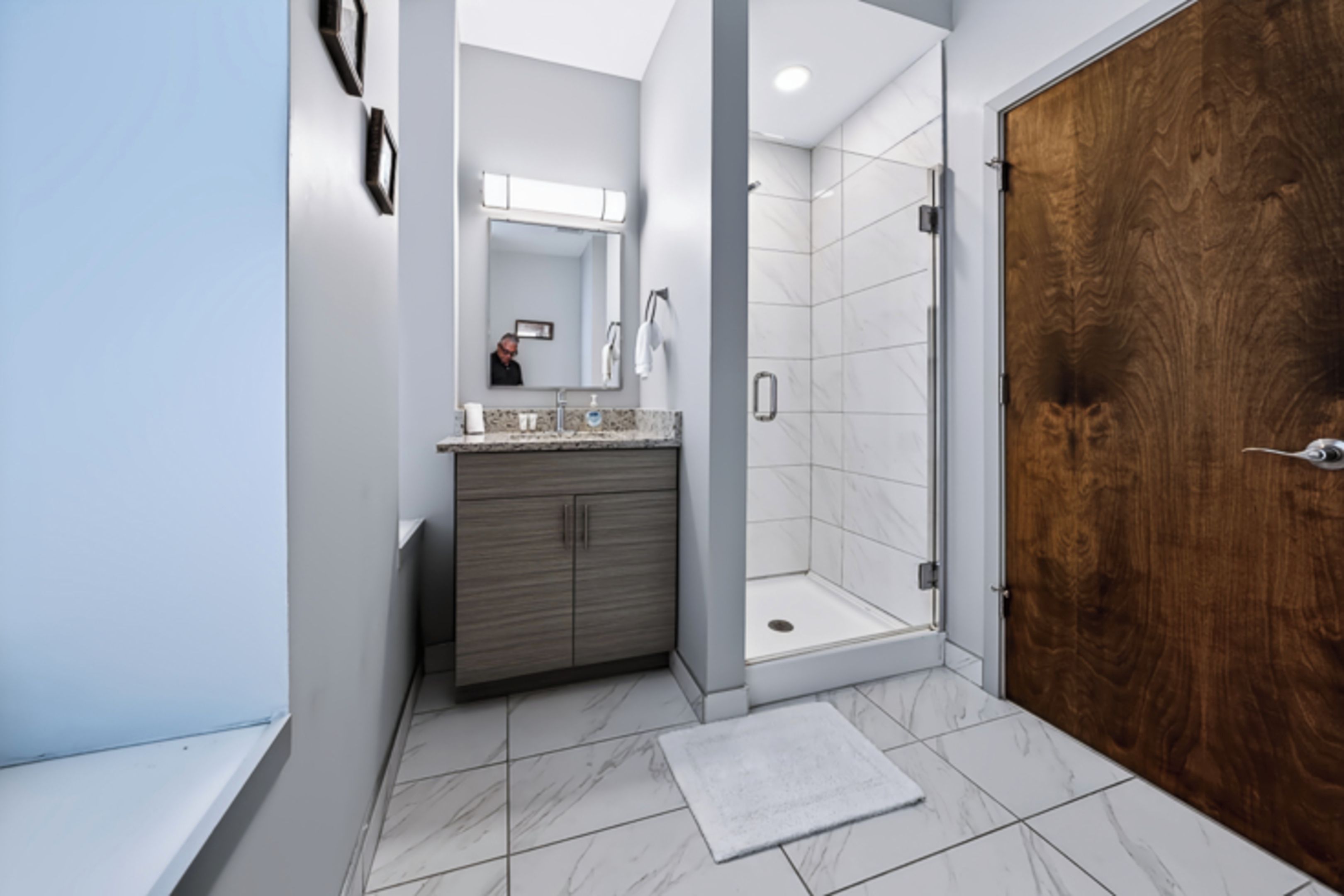 A modern bathroom with a wooden door, a shower, and a vanity with a mirror.