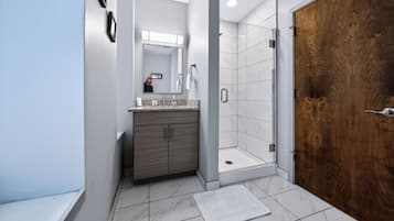 A modern bathroom with a wooden door, a shower, and a vanity with a mirror.