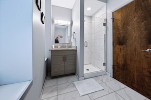 A modern bathroom with a wooden door, a shower, and a vanity with a mirror. - Downtown Historic Warehouse District Lofts 206 (Cleveland)