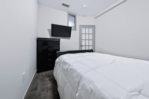 A bedroom with a bed, a dresser, a television mounted on the wall, and a door. - Downtown Historic Warehouse District Lofts 206 (Cleveland)
