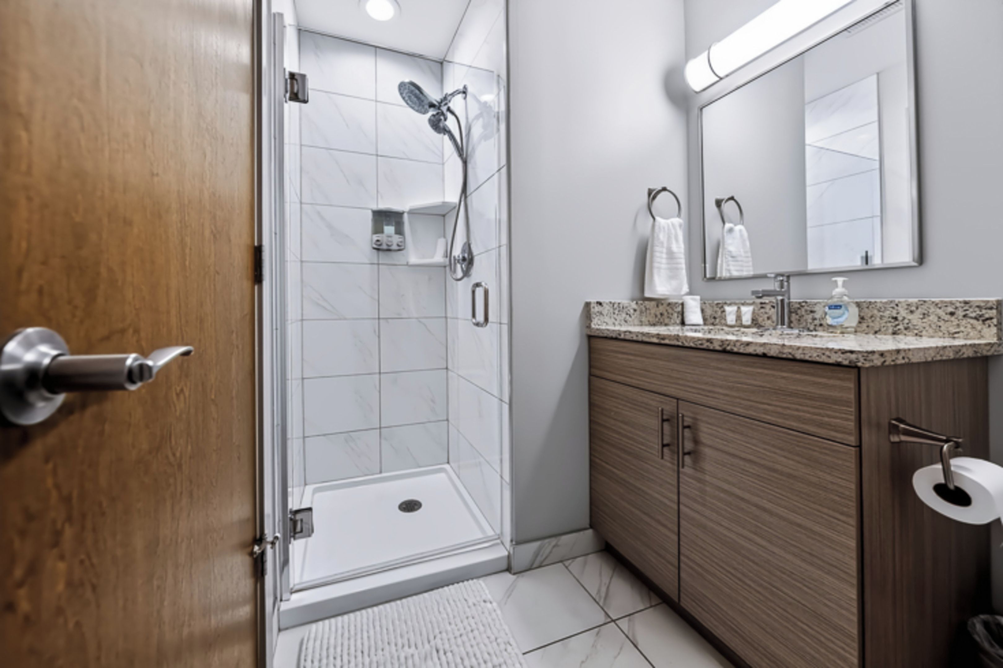 A modern bathroom with a glass shower enclosure, a wooden vanity, and a large mirror.