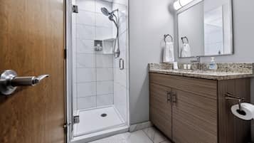 A modern bathroom with a glass shower enclosure, a wooden vanity, and a large mirror.