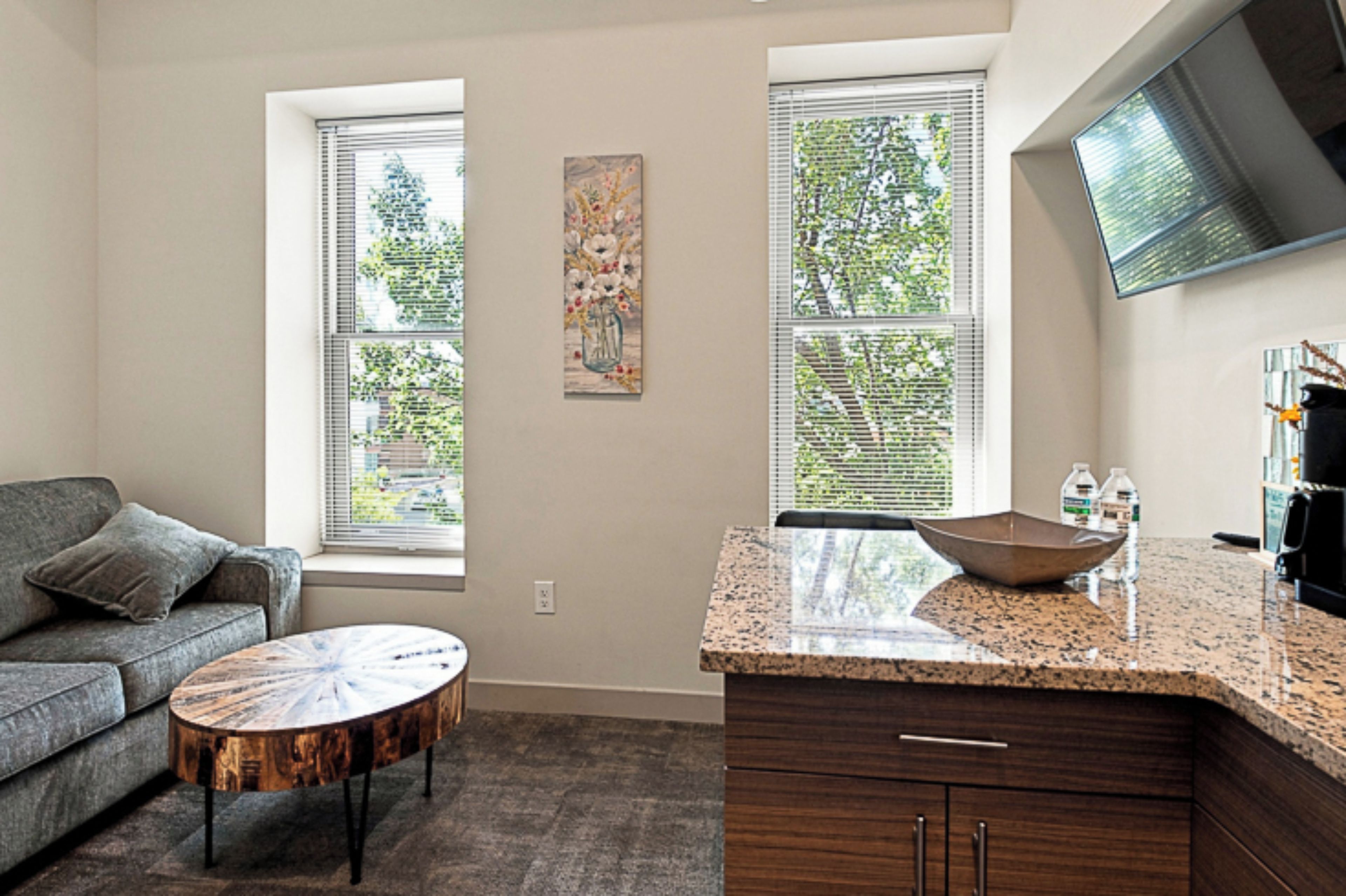 A modern kitchen with a granite countertop, wooden cabinets, and a large window with blinds.