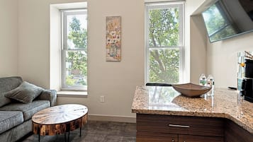 A modern kitchen with a granite countertop, wooden cabinets, and a large window with blinds.