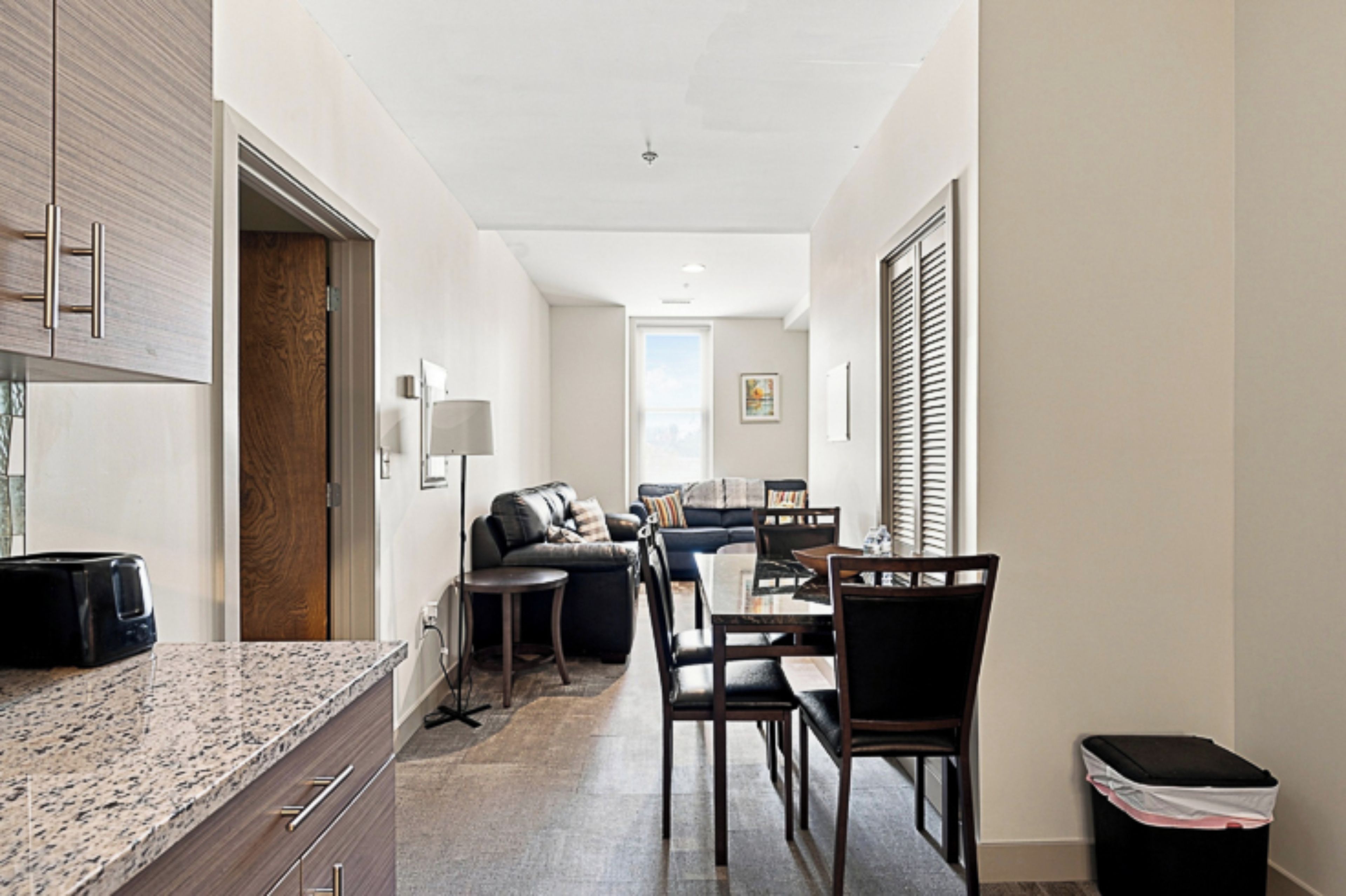 A modern kitchen with granite countertops, a wooden door, and a dining area with a table and chairs.
