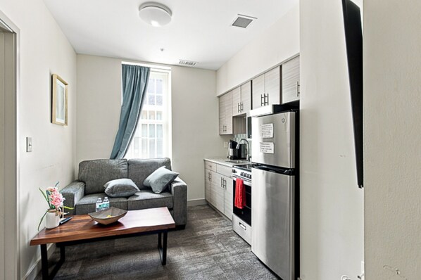 A compact living space with a kitchenette, a sofa, a dining table, and a window with curtains.