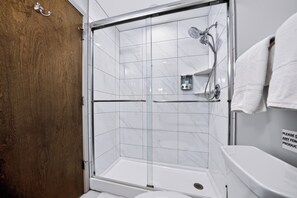 A shower area with a glass door, a white toilet, and a wooden door.