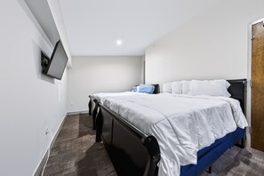 A bedroom with a bed, a flat-screen TV mounted on the wall, and a door.