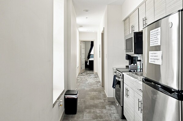 A narrow kitchen with stainless steel appliances, a trash bin, and a microwave.